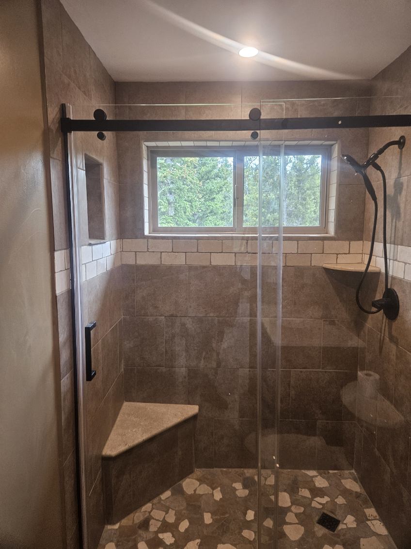 Tiled walk-in shower with glass door, bench and window by A1M Construction